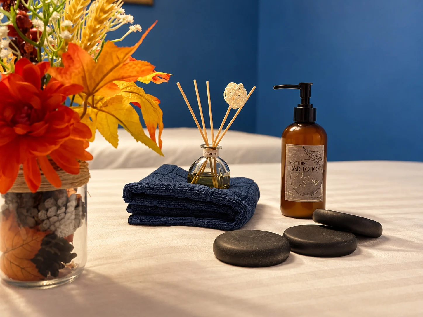 Folded towel, reed diffuser, lotion and smooth stones on a massage table at the Gainesville studio